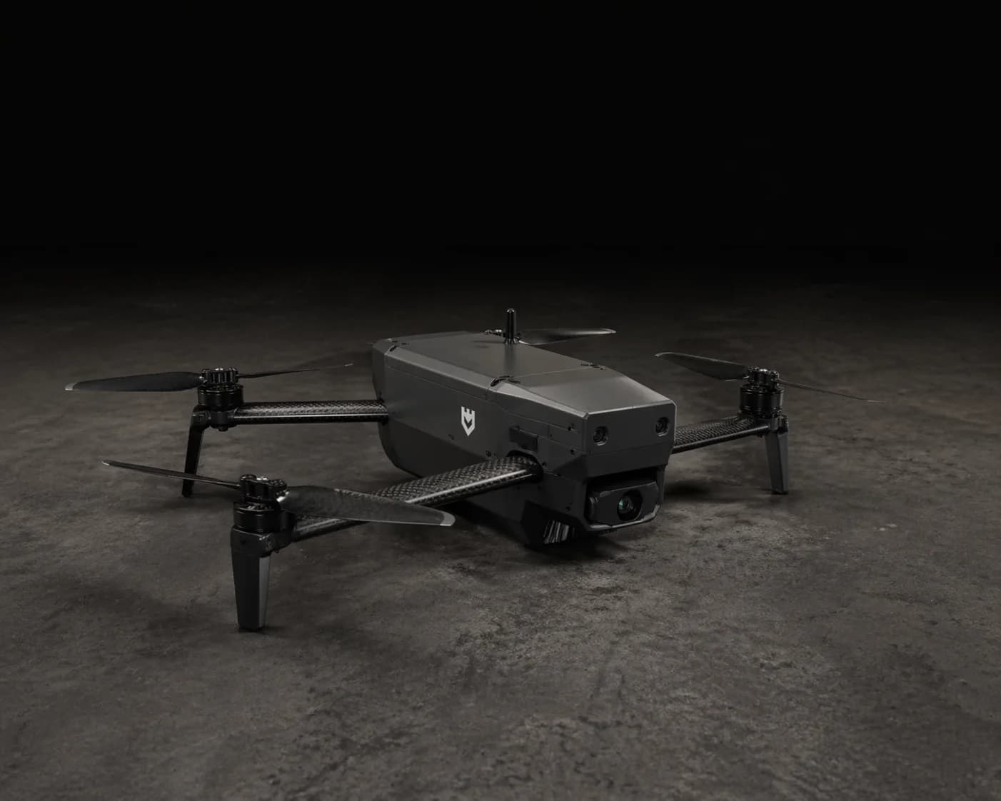 Grayhaven unmanned aerial system, low-profile quadcopter with carbon-fiber propellers, folding landing legs, and nose-mounted gimbal EO camera on a dark studio floor
